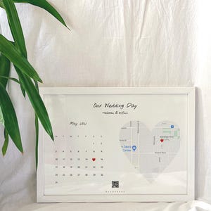 Può includere: Una stampa incorniciata bianca con un calendario per maggio 2021, con un cuore rosso che segna l'8. La stampa presenta anche una mappa di una città con un cuore rosso che segna una posizione. Il testo "Our Wedding Day Melissa & Erfan" è in cima alla stampa.