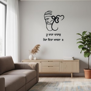 Könnte beinhalten: Schwarze Wandkunst mit einer stilisierten Sikh-Figur mit Bart und Turban, begleitet von Text in einer Schrift. Das Kunstwerk ist an einer hellgrauen Wand über einem Holzschrank angebracht. Eine Topfpflanze und dekorative Gegenstände sind ebenfalls zu sehen.