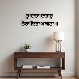 May include: A dark brown wooden console table with two drawers and a lower shelf, holding books. A small potted plant and a modern lamp with a white shade sit on the table. Above, black text is displayed on the white wall.