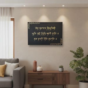 Könnte beinhalten: Ein schwarzes, rechteckiges Wandkunstwerk mit goldenem Text und dekorativen Eckdesigns. Der Text ist in einer Schriftart gehalten. Die Kunst wird in einem Wohnzimmer über einem Holzschrank ausgestellt.