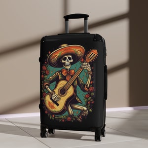 May include: Black suitcase with a colorful illustration of a skeleton wearing a sombrero and playing a guitar. The skeleton is surrounded by flowers and leaves.
