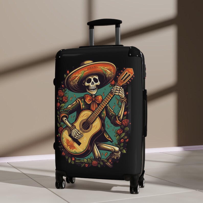 May include: Black suitcase with a colorful illustration of a skeleton wearing a sombrero and playing a guitar. The skeleton is surrounded by flowers and leaves.