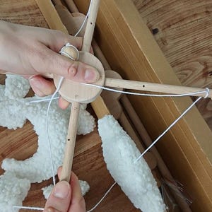 May include: A wooden baby mobile frame featuring a central circular hub with four extending arms, each ending in a small wooden sphere. White, textured, cloud-shaped fabric pieces are suspended from the frame by thin white strings.