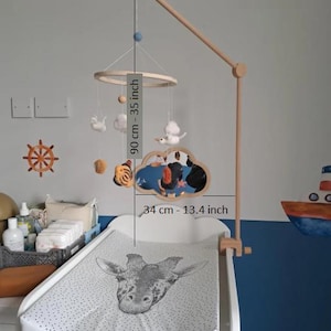 May include: A wooden baby mobile featuring felt figures of a tiger, a cloud, and a ship, suspended from a circular frame on a wooden arm. The mobile measures 35 inches in total height and 13.4 inches in width, hanging over a changing pad.