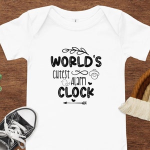 May include: White baby onesie with black text that reads "WORLD'S cutest alarm CLOCK" with a small bird, infinity symbol, and pacifier graphic.