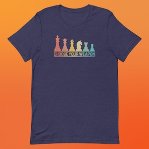 May include: A navy blue t-shirt with a vintage-style graphic of chess pieces in rainbow colors. The text "CHOOSE YOUR WEAPON" is printed below the chess pieces.