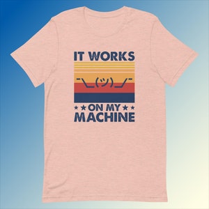Puede incluir: Una camiseta rosa con un gráfico de estilo retro que dice "IT WORKS ( ͡° ͜ʖ ͡°) ON MY MACHINE".