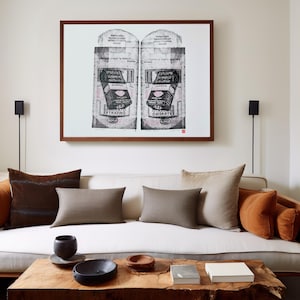 Könnte beinhalten: Ein weißes Sofa mit braunen, beigen und orangen Kissen. Über dem Sofa hängt ein gerahmtes Schwarzweißbild einer Vintage-Schokoladenverpackung. Ein Holz-Couchtisch mit einer schwarzen Schale, einer Holzschale und einem Buch steht vor dem Sofa.