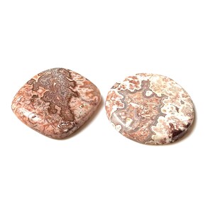 May include: Two polished gemstones with intricate patterns. One is square-shaped, the other is oval. Both stones feature a mix of brown, white, and reddish-pink hues, creating a marbled effect. The gemstones are set against a white background.