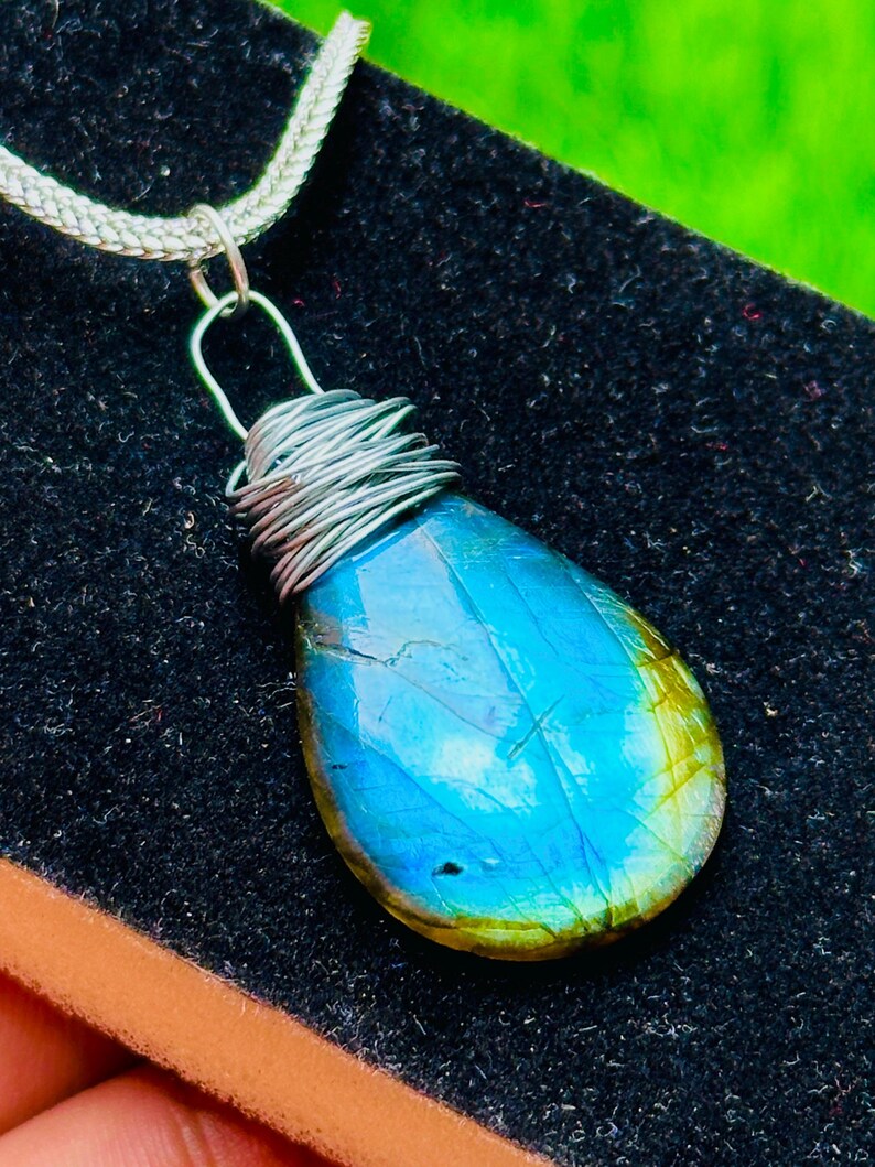 May include: A teardrop-shaped pendant with a vibrant blue and green gemstone, wrapped in silver wire. The pendant hangs from a silver chain, creating a striking contrast against the dark background. This unique piece is a beautiful accessory.