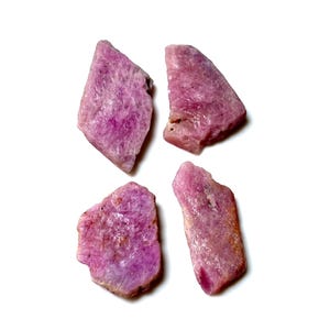 Könnte beinhalten: Vier grob geschnittene, natürliche rosa Edelsteine ​​werden vor einem weißen Hintergrund gezeigt. Die Steine ​​variieren in Form und Größe, mit einer Reihe von Rosatönen und sichtbaren Texturen. Diese rohen Kristalle sind ideal für die Schmuckherstellung oder das Sammeln.
