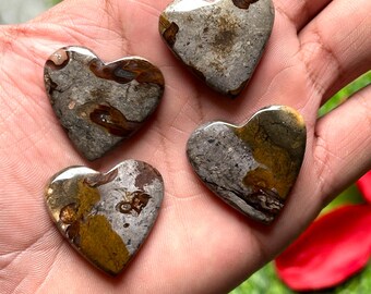 Puede incluir: Cuatro piedras en forma de corazón con un acabado pulido. Las piedras tienen una mezcla de colores grises, marrones y beige, con patrones únicos. Los corazones se sostienen en una mano, con un fondo verde.