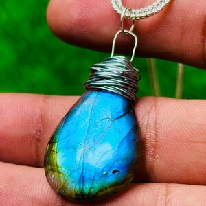 May include: A teardrop-shaped labradorite pendant necklace. The iridescent blue and green stone is wrapped in silver wire and suspended from a silver chain. The pendant is approximately 1.5 inches long.