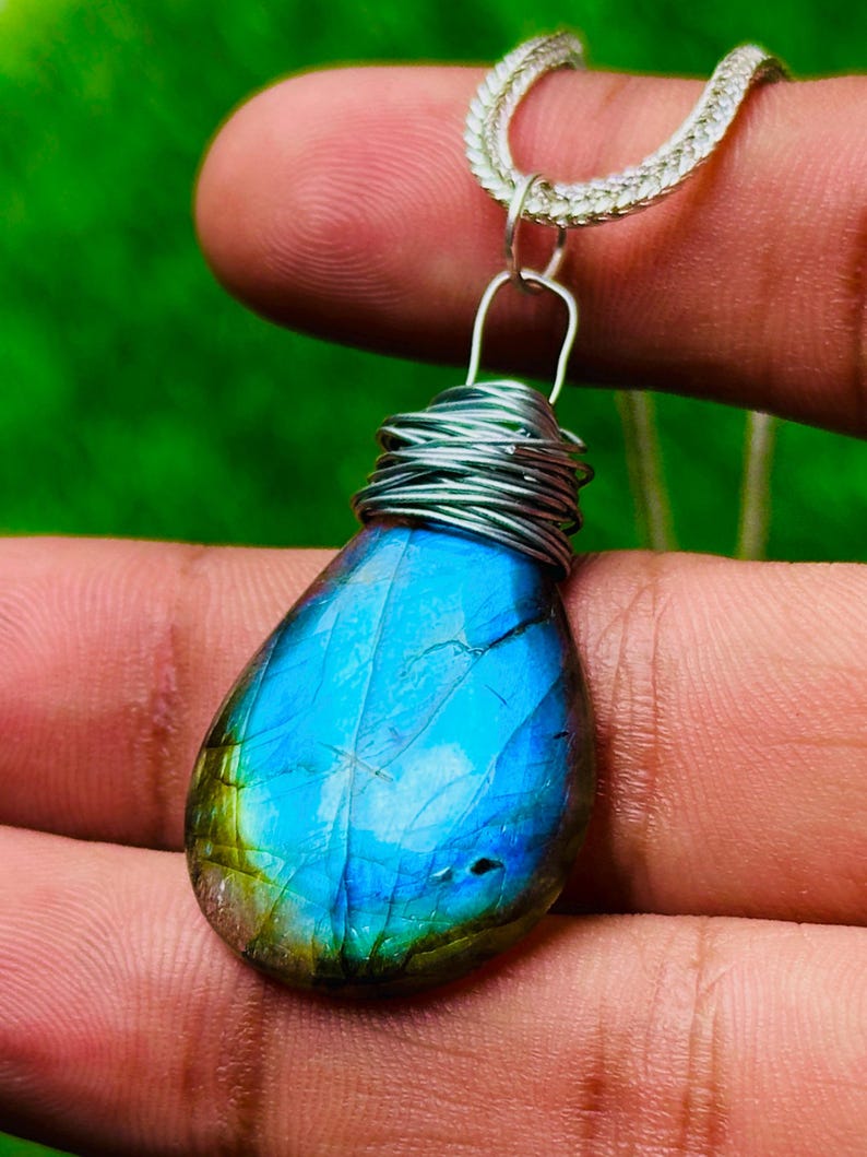 May include: A teardrop-shaped labradorite pendant necklace. The iridescent blue and green stone is wrapped in silver wire and suspended from a silver chain. The pendant is approximately 1.5 inches long.