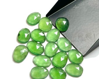 Op de afbeelding: Een verzameling gefacetteerde, ovaalvormige groene edelstenen. De edelstenen hebben een heldere, lichtgroene kleur en een gepolijst, reflecterend oppervlak. Ze liggen op een wit oppervlak, met een zwarte bak op de achtergrond.