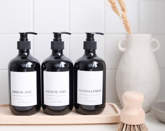 May include: Three black pump bottles with white labels reading "Dish Wash", "Hand Wash", and "Hand Lotion". The bottles sit on a wooden tray, next to a white vase with wheat stalks and a wooden brush. Each bottle holds 16.9 fl oz.