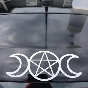 May include: White vinyl decal featuring a triple moon symbol with a pentagram in the center. The design is a crescent moon on each side of a circle containing a five-pointed star. The decal is on a black surface.
