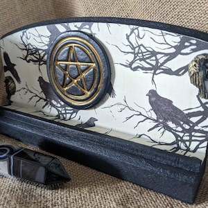 May include: A white ceramic mug with a black handle and the text "But First, Coffee" in a black, handwritten-style font. The mug is on a white surface.