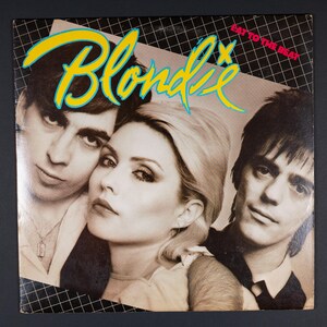 May include: Album cover for Blondie's "Eat to the Beat." The cover features three band members in a sepia tone, with the band's name in yellow and blue stylized text. The album title is in red text.