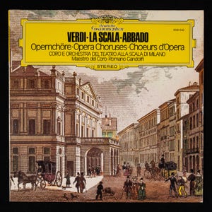 May include: A yellow record album cover with a black and white illustration of the Teatro alla Scala opera house in Milan, Italy. The text on the cover reads "VERDI-LA SCALA-ABBADO" and "Opernchöre Opera Choruses Choeurs d'Opera".