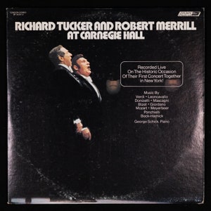 May include: A black and white album cover featuring a photo of two men in suits singing. The album title is "Richard Tucker and Robert Merrill at Carnegie Hall". The album cover also includes the text "Recorded Live On The Historic Occasion Of Their First Concert Together in New York!" and "Music By Verdi Leoncavallo Donizetti Mascagni Bizet Giordano Mozart Meyerbeer Ponchielli Bock-Harnick George Schick, Piano".
