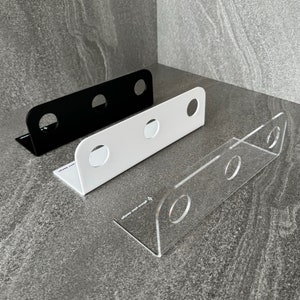 Może przedstawiać: Trzy organizatory ścienne w kolorze czarnym, białym i przezroczystym akrylu. Każdy organizer ma trzy otwory do przechowywania przedmiotów.