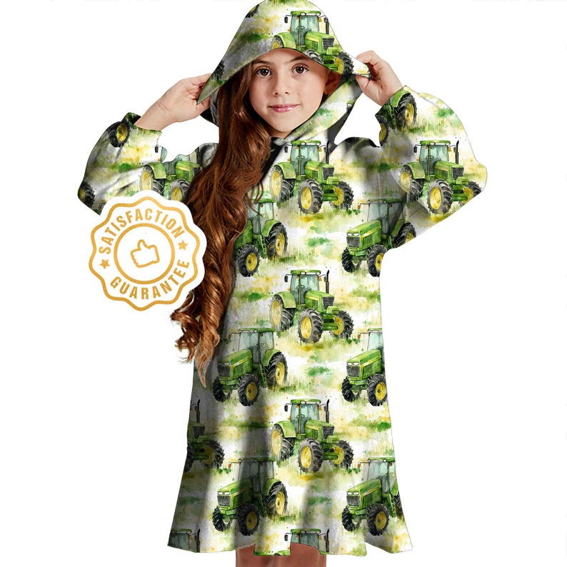 May include: A white hooded dress with a green tractor print. The dress has long sleeves and a drawstring hood. The text "Satisfaction Guarantee" is printed on a gold star.