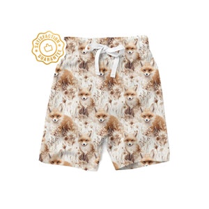 May include: White shorts with a repeating pattern of brown foxes and beige foliage. The shorts have a white drawstring.