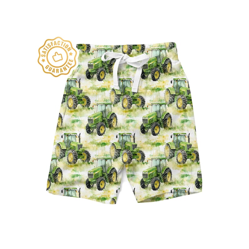 May include: White shorts with a green tractor pattern. The tractors are painted in a watercolour style and are scattered across the fabric. The shorts have a white drawstring.