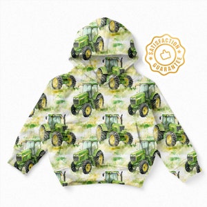 May include: A white hooded sweatshirt with a green and yellow watercolour pattern of tractors. The sweatshirt has a gold satisfaction guarantee label with a thumbs up icon.