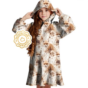 May include: A white hooded dress with a fox print. The dress has long sleeves and a loose fit. The hood is lined with a brown fabric. The dress has a brown and white fox print all over. The dress has a white background with brown foxes and flowers.