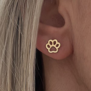 May include: A pair of gold-toned stud earrings featuring a paw print design.