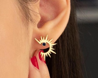 Könnte beinhalten: Goldfarbene Ohrringe in Form eines Sonnenaufgangs mit einem kleinen, dunkelblauen Stein in der Mitte. Die Ohrringe haben ein stacheliges Design und werden am Ohr getragen. Das Bild zeigt eine Nahaufnahme der Ohrringe.