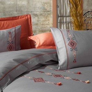 Peut inclure: Literie grise avec un motif géométrique brodé en rouge et blanc. La literie est ornée de pompons et est fabriquée dans un tissu doux et confortable.