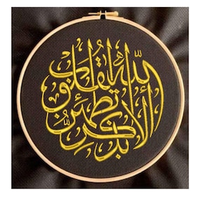 Pode incluir: Um aro de bordado preto com um desenho de caligrafia árabe bordado em ouro. O desenho é um padrão circular de escrita intrincada.