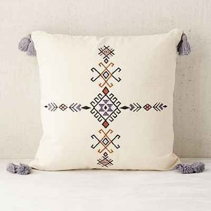 May include: A white throw pillow with a geometric pattern in shades of orange, red, purple, and black. The pillow has tassels on each corner.