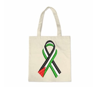 Puede incluir: Una bolsa de tela blanca con un diseño de cinta verde, negra y roja. La cinta tiene forma de signo de paz.
