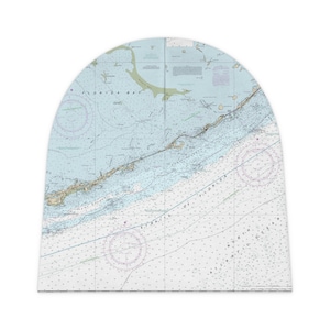May include: A beanie hat featuring a nautical chart design of the Florida Keys. The map is in shades of blue, green, and white, with detailed lines and text indicating geographical features and ocean depths. The hat has a curved top.