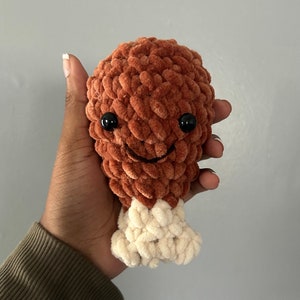 May include: A crocheted plush toy shaped like a chicken leg. The leg is brown and the bone is white. The toy has a smiling face with black eyes.