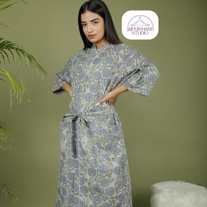 Puede incluir: Bata gris con estampado floral, cintur&oacute;n a juego y bolsillos. La bata tiene un ribete blanco y llega hasta la rodilla. Las mangas son de tres cuartos. La bata est&aacute; hecha de una tela suave y ligera. El logotipo "JAIPUR HAND STUDIO" est&aacute; en la esquina superior derecha.