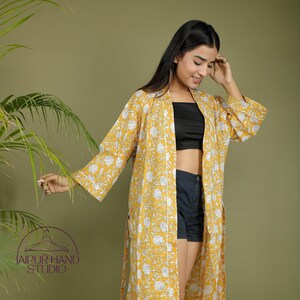 May include: A long yellow floral print robe with white trim and a tie belt. The robe is open and worn over a black crop top and dark blue denim shorts.