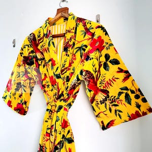 May include: A yellow velvet robe with a floral print featuring red flowers, green leaves, and birds. The robe has a tie belt and long sleeves.