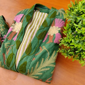 May include: A green embroidered jacket with a floral design. The jacket has a striped lining and a tie closure.