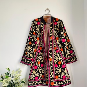 Può includere: Una giacca nera ricamata con un motivo floreale rosa, arancio e oro. La giacca ha un colletto alla coreana e maniche lunghe.