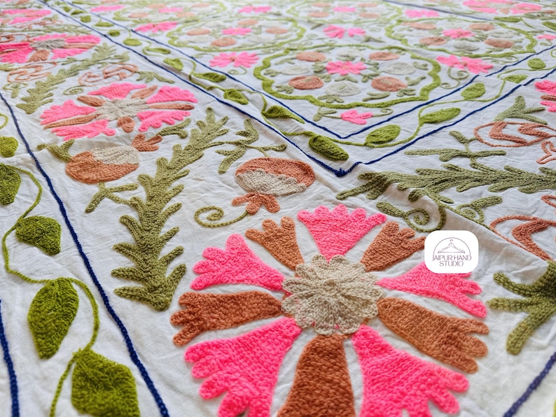 May include: White cotton fabric with intricate embroidery in pink, green, and brown. The design features floral motifs and leaves, creating a delicate and intricate pattern. The fabric is hand-stitched and has a textured surface.