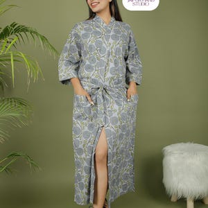 Puede incluir: Una bata gris con estampado floral, cintur&oacute;n anudado y bolsillos. La bata presenta un patr&oacute;n repetido de flores grises y hojas verdes. La bata llega a la rodilla y tiene una abertura en la parte delantera. El logo de la marca est&aacute; en la esquina superior derecha.