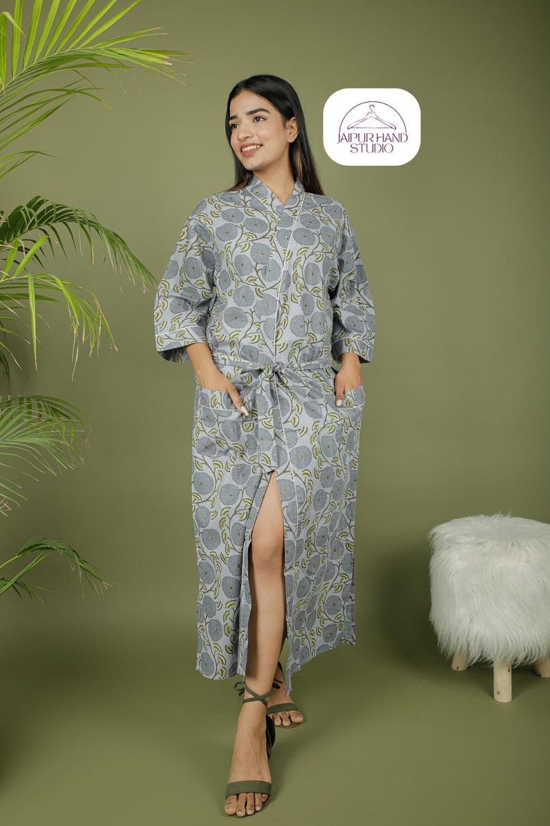 Puede incluir: Una bata gris con estampado floral, cintur&oacute;n anudado y bolsillos. La bata presenta un patr&oacute;n repetido de flores grises y hojas verdes. La bata llega a la rodilla y tiene una abertura en la parte delantera. El logo de la marca est&aacute; en la esquina superior derecha.