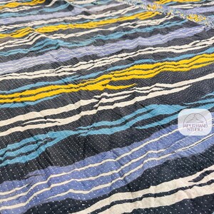 May include: A blue, yellow, and white striped fabric with a subtle dotted pattern. The fabric is wrinkled and has a textured surface.