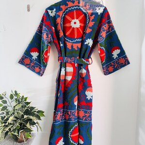 May include: A blue cotton robe with a floral embroidery pattern in red, pink, and white. The robe has a belt and long sleeves.