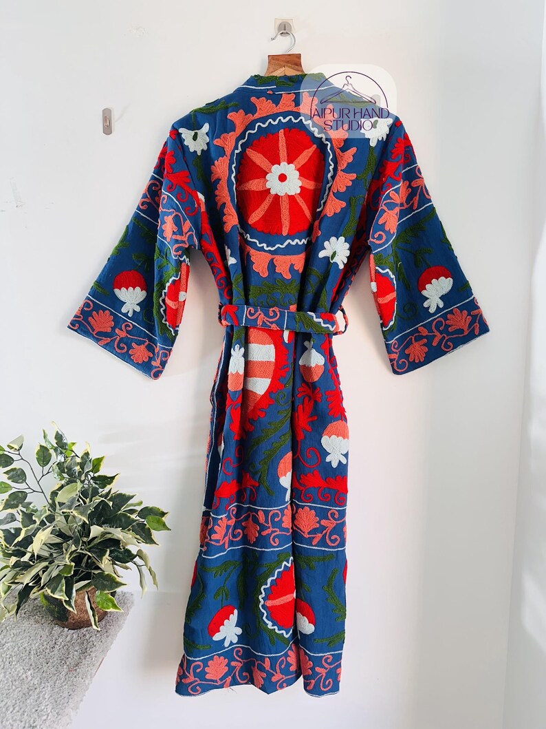 May include: A blue cotton robe with a floral embroidery pattern in red, pink, and white. The robe has a belt and long sleeves.